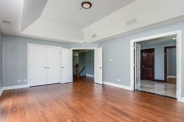 unfurnished bedroom with a closet, a tray ceiling, and hardwood / wood-style flooring