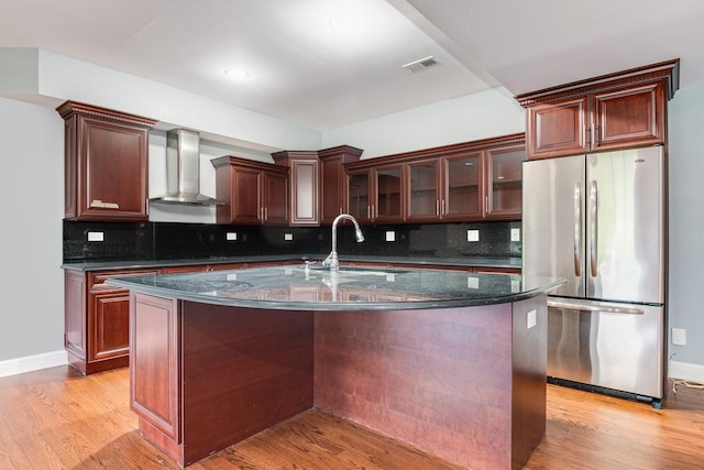 kitchen featuring a kitchen island with sink, sink, wall chimney exhaust hood, light hardwood / wood-style floors, and stainless steel refrigerator