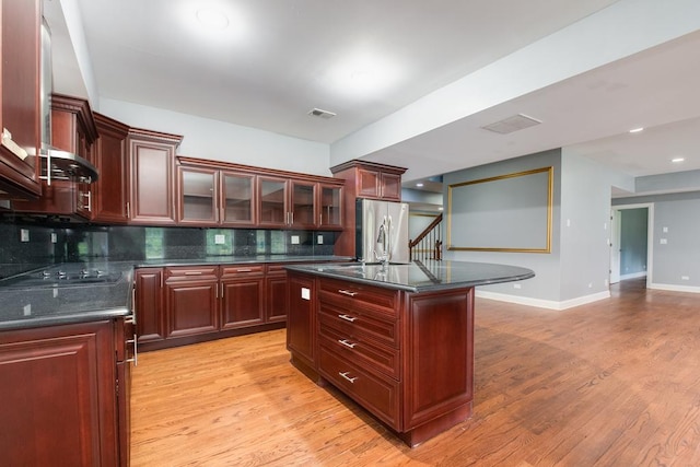 kitchen with backsplash, a kitchen island with sink, stainless steel refrigerator, and black cooktop