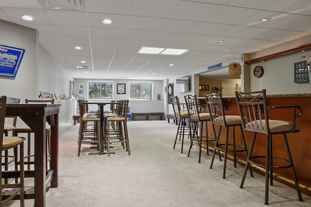 dining room with a paneled ceiling, light carpet, and indoor bar