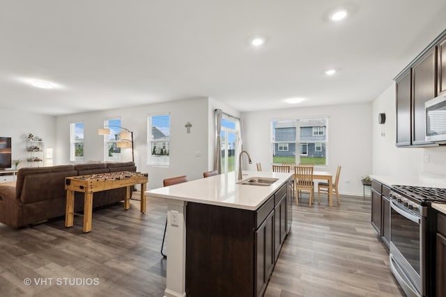 kitchen with light wood-type flooring, stainless steel gas range oven, dark brown cabinetry, sink, and an island with sink