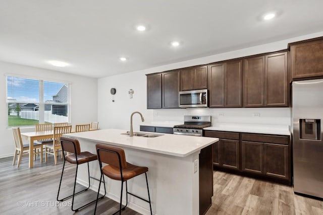 kitchen featuring dark brown cabinetry, sink, stainless steel appliances, and a center island with sink