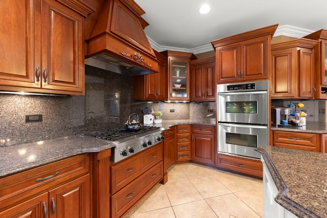 kitchen featuring custom exhaust hood, ornamental molding, appliances with stainless steel finishes, and dark stone countertops