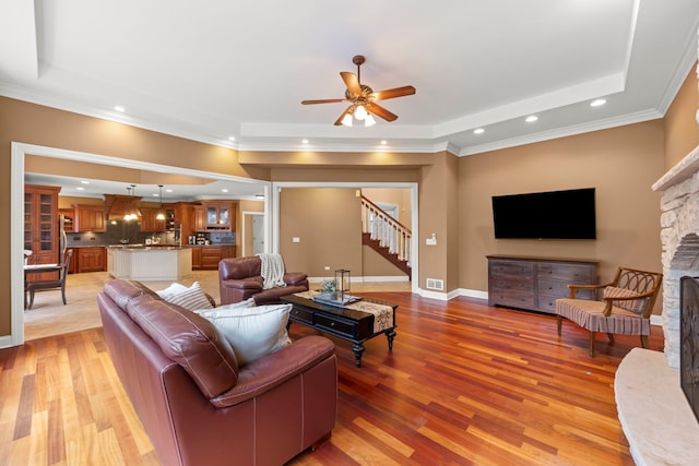 living room with a stone fireplace, a raised ceiling, and light wood-type flooring