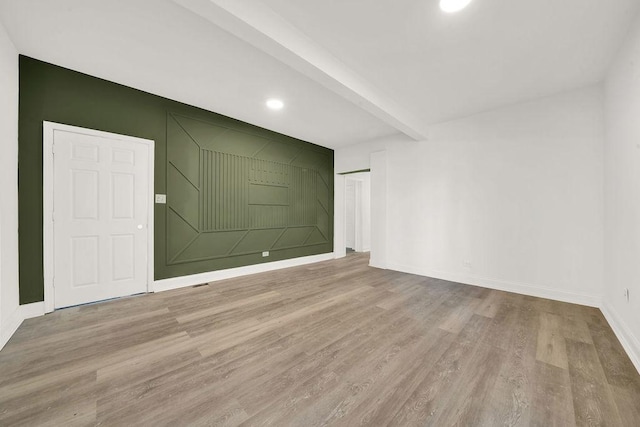 empty room with beam ceiling and light wood-type flooring