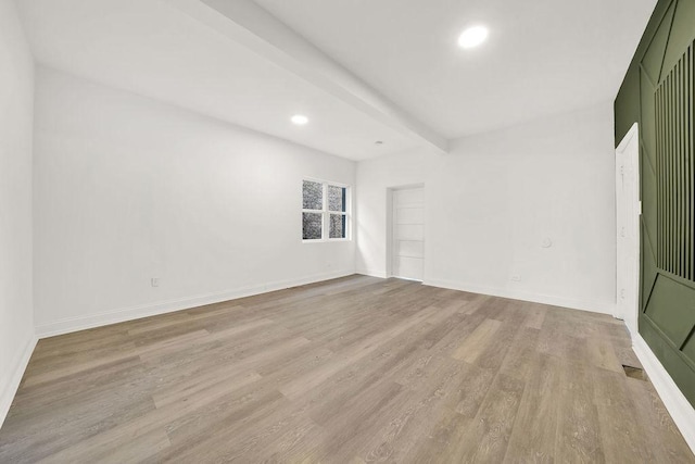 empty room with beam ceiling and light wood-type flooring