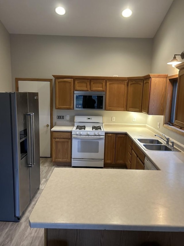 kitchen featuring kitchen peninsula, sink, stainless steel appliances, and light hardwood / wood-style flooring