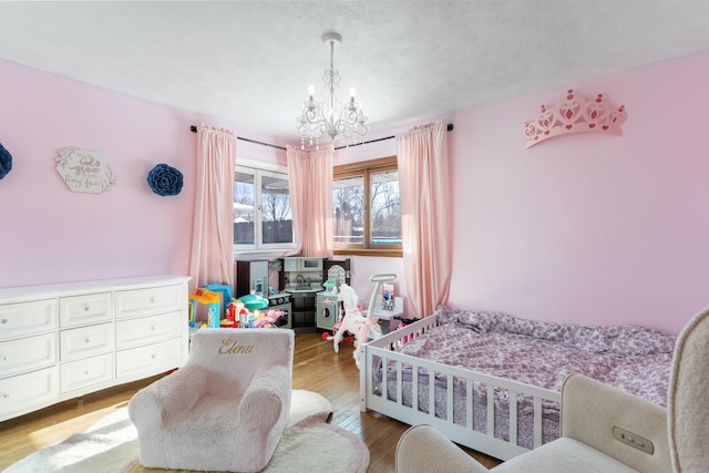 bedroom featuring a crib, a textured ceiling, light hardwood / wood-style floors, and an inviting chandelier