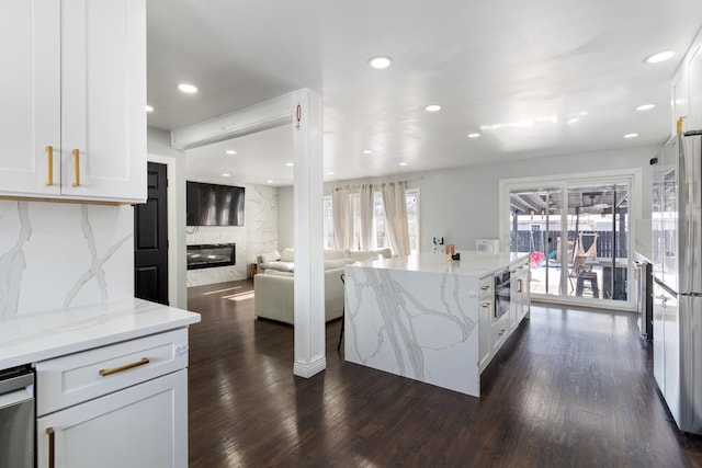 kitchen with appliances with stainless steel finishes, light stone counters, a fireplace, dark hardwood / wood-style floors, and white cabinetry