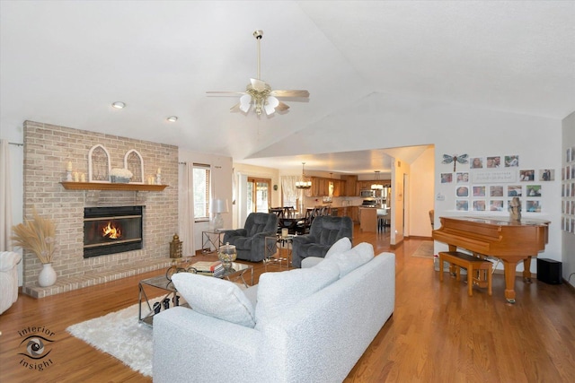 living room with ceiling fan, vaulted ceiling, a brick fireplace, and light wood-type flooring