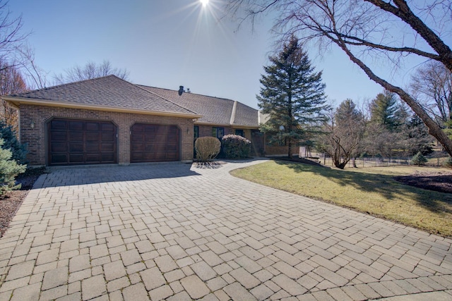 view of front facade featuring brick siding, a shingled roof, a front yard, decorative driveway, and a garage