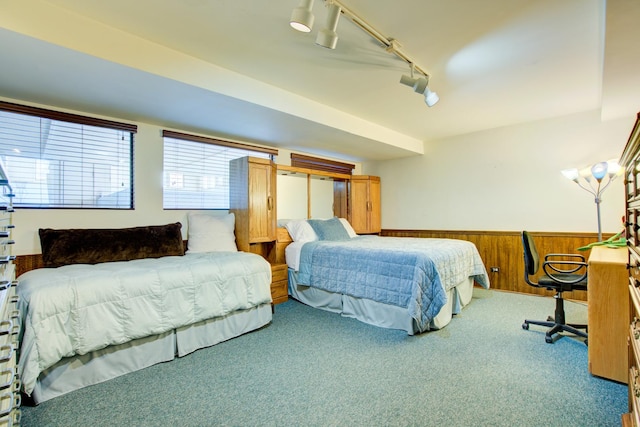 carpeted bedroom featuring a wainscoted wall, wooden walls, and track lighting