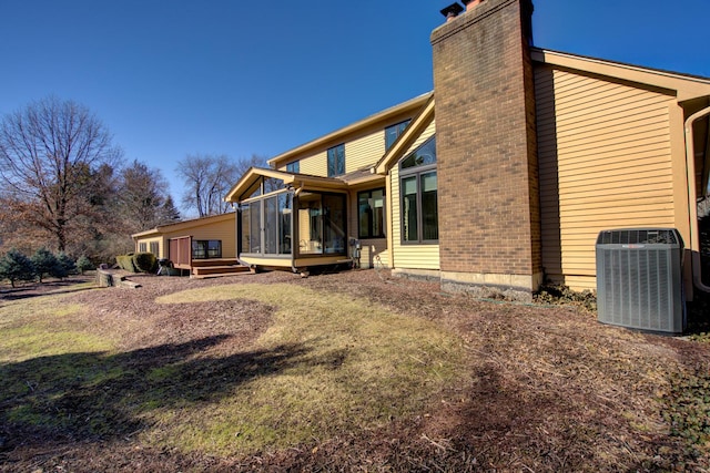 rear view of property featuring central air condition unit, a deck, a chimney, and a sunroom