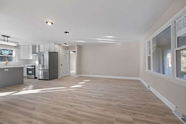 kitchen with decorative backsplash, white cabinetry, light hardwood / wood-style floors, and appliances with stainless steel finishes