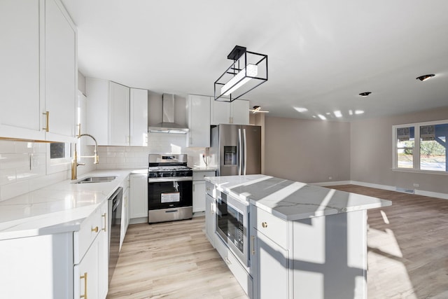 kitchen with stainless steel appliances, a kitchen island, wall chimney exhaust hood, white cabinetry, and backsplash