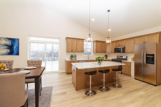 kitchen with light wood-type flooring, stainless steel appliances, decorative light fixtures, high vaulted ceiling, and a center island