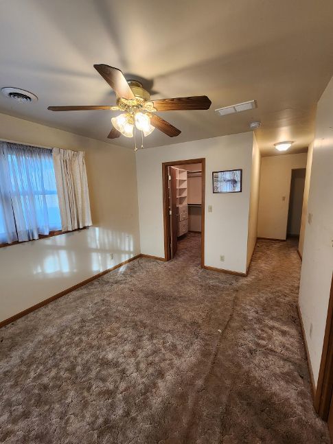 empty room with carpet floors, baseboards, visible vents, and ceiling fan