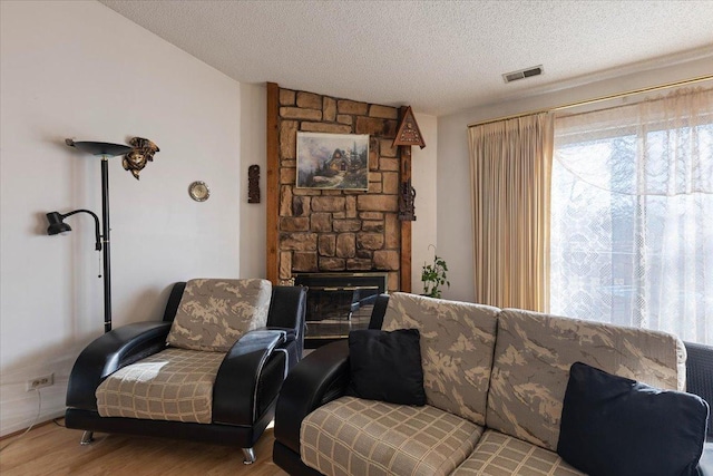 living room featuring a textured ceiling, light hardwood / wood-style flooring, and a stone fireplace