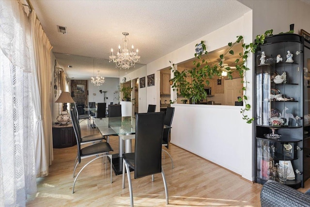 dining space with a textured ceiling, light wood-type flooring, and a chandelier