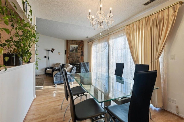 dining room featuring a notable chandelier, light hardwood / wood-style flooring, a fireplace, and a textured ceiling