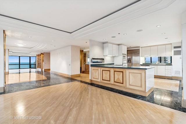 kitchen featuring light brown cabinets, a kitchen island with sink, white cabinets, a raised ceiling, and built in appliances