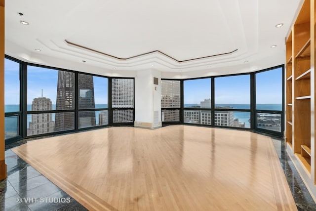 interior space with hardwood / wood-style floors, a water view, a raised ceiling, and a wall of windows