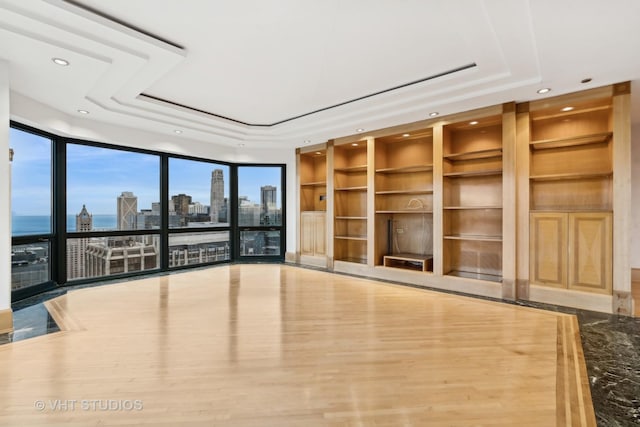 unfurnished living room featuring hardwood / wood-style floors, built in shelves, floor to ceiling windows, and a tray ceiling