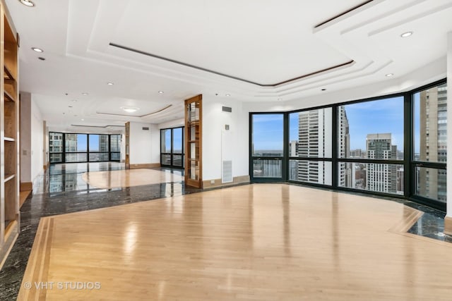 unfurnished room with expansive windows, a raised ceiling, wood-type flooring, and a healthy amount of sunlight