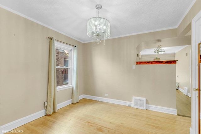 empty room featuring wood-type flooring, ornamental molding, a textured ceiling, and a chandelier