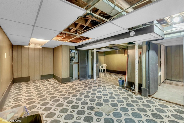 basement featuring a paneled ceiling and wood walls