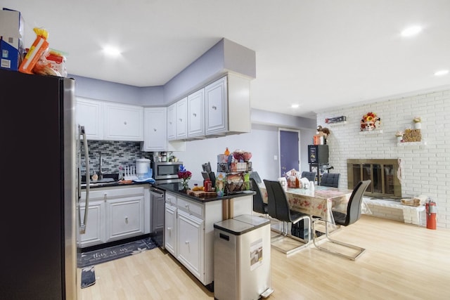 kitchen featuring appliances with stainless steel finishes, decorative backsplash, kitchen peninsula, a brick fireplace, and light hardwood / wood-style flooring