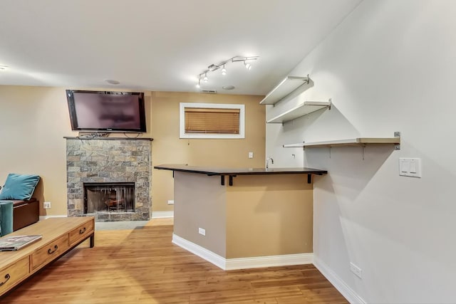 kitchen featuring kitchen peninsula, light wood-type flooring, rail lighting, a fireplace, and a breakfast bar area