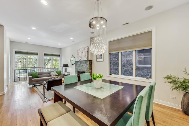 dining room featuring a fireplace, light wood-type flooring, and a notable chandelier