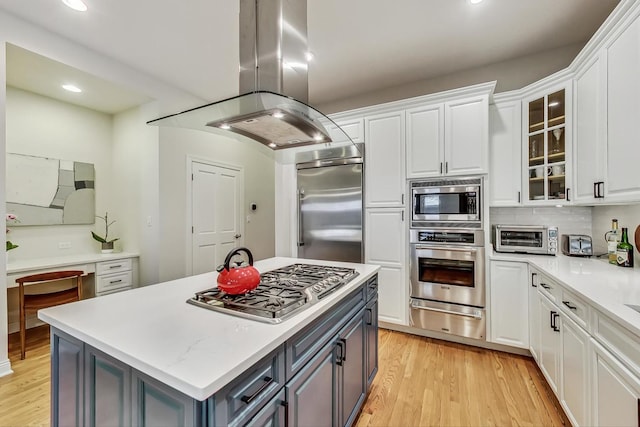 kitchen with white cabinetry, a center island, built in appliances, island exhaust hood, and decorative backsplash