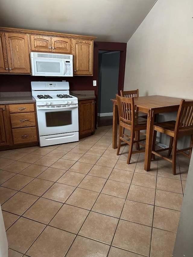 kitchen featuring lofted ceiling, light tile patterned flooring, and white appliances