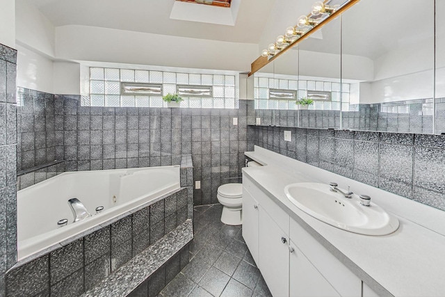 bathroom featuring vanity, toilet, tiled tub, and tile walls