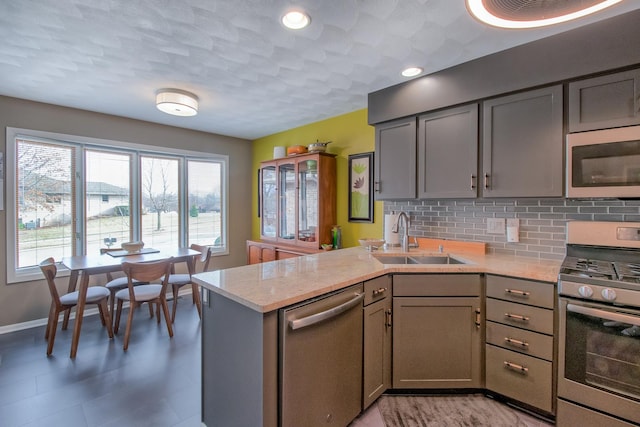 kitchen featuring sink, decorative backsplash, gray cabinets, kitchen peninsula, and stainless steel appliances