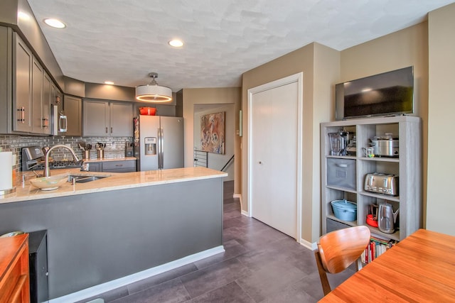 kitchen with kitchen peninsula, appliances with stainless steel finishes, tasteful backsplash, sink, and pendant lighting