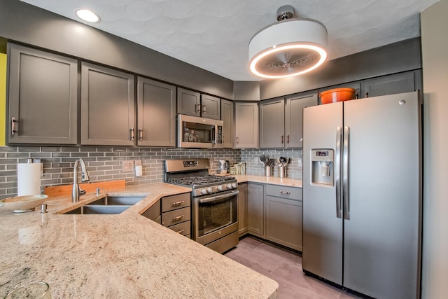 kitchen with backsplash, light stone counters, sink, and stainless steel appliances