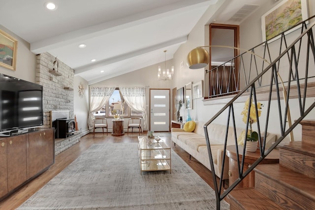 living room with hardwood / wood-style flooring, a wood stove, an inviting chandelier, and lofted ceiling with beams