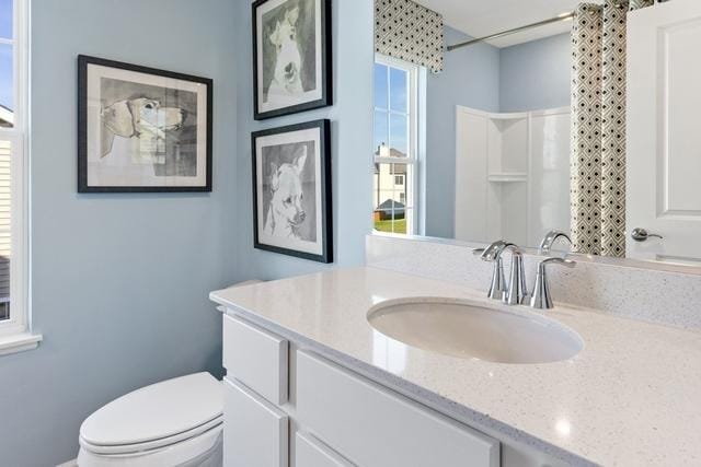 bathroom with walk in shower, vanity, and toilet