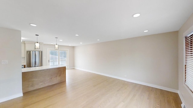 kitchen featuring light wood-type flooring, decorative light fixtures, white cabinetry, and stainless steel refrigerator