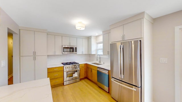 kitchen with white cabinets, appliances with stainless steel finishes, tasteful backsplash, sink, and light hardwood / wood-style flooring