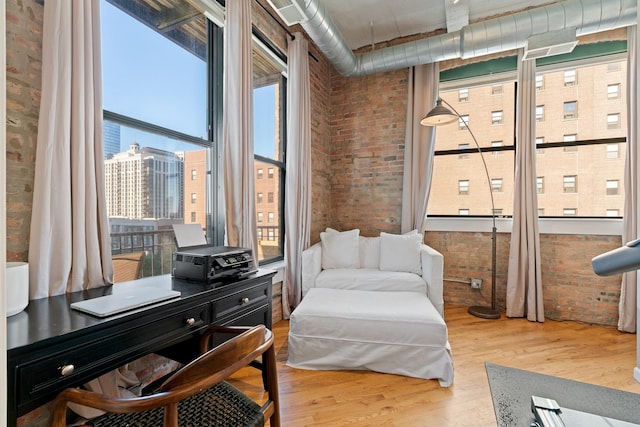 living area with light hardwood / wood-style floors, brick wall, and a healthy amount of sunlight