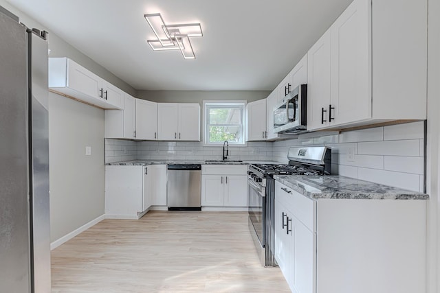 kitchen with white cabinetry, sink, tasteful backsplash, light stone counters, and appliances with stainless steel finishes