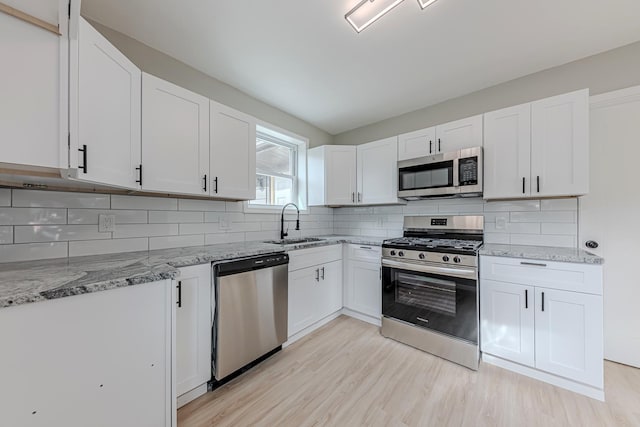 kitchen with white cabinets, appliances with stainless steel finishes, light stone counters, and sink