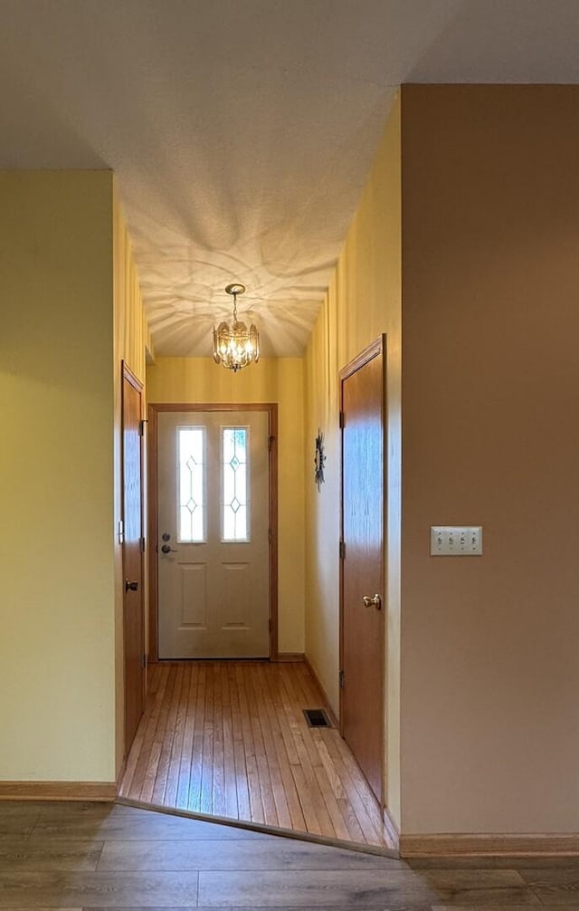 doorway to outside featuring a chandelier, visible vents, baseboards, and hardwood / wood-style flooring