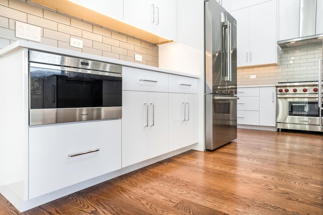 kitchen with light wood-type flooring, backsplash, exhaust hood, high quality appliances, and white cabinets