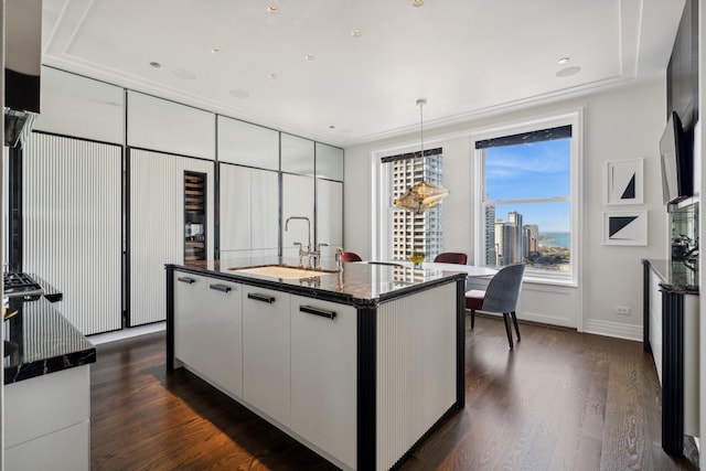 kitchen with dark stone counters, a center island with sink, white cabinets, sink, and hanging light fixtures