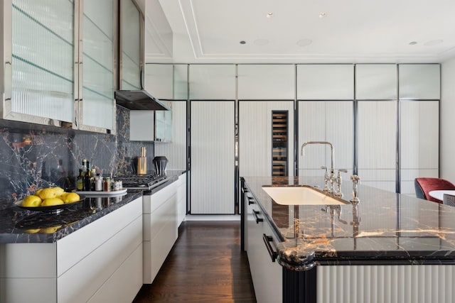 kitchen with dark hardwood / wood-style flooring, wall chimney range hood, sink, white cabinets, and a large island